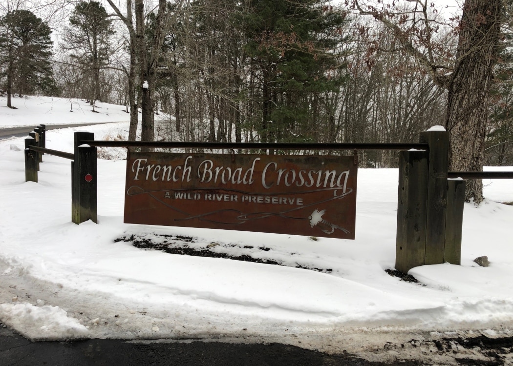 French broad crossing community sign in snow by oak tree trunks